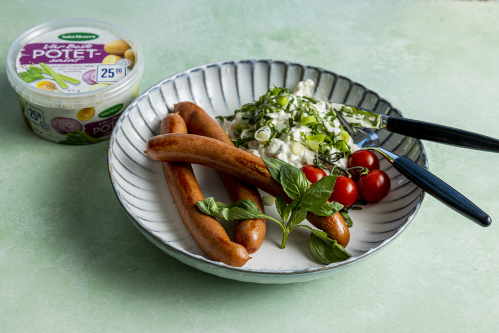 Bilde-av-en-tallerken-med-pølser-potetsalat-og-tomater-toppet-med-vårløk-og-bailikum